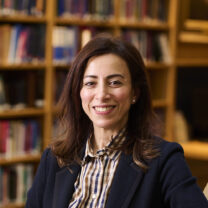 Amira smiles, with her hair down and books in the background