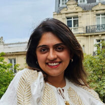 Sahhna smiles wearing a white blouse with Parisian houses and trees behind