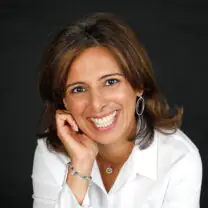 Neelam Sharma smiles in front of a dark background