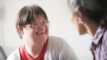 How to overcome barriers to effective consultation with adults with learning disabilities and practical ways to improve pharmacy consultation skills. In the image, an adult with Down’s syndrome speaks with a consultant