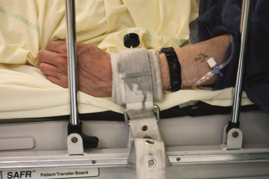 Challenging behaviour is any non-verbal, verbal of physical behaviour which makes it difficult to deliver good care safely. It includes grabbing, biting, punching, or self-injury. In the image, an aggressive patient is restrained to a hospital bed