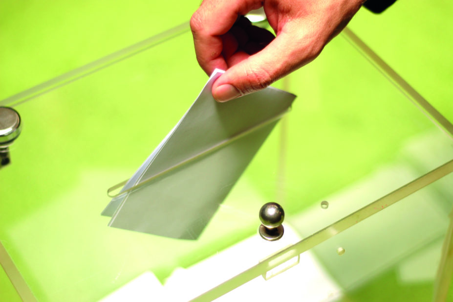 Close up of hand putting vote in ballot box