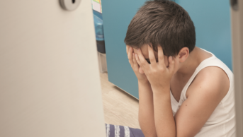 Child in a corner with his eyes covered