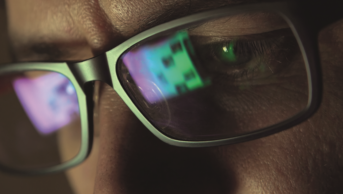 Close up of computer screen reflected on a man's eyeglasses
