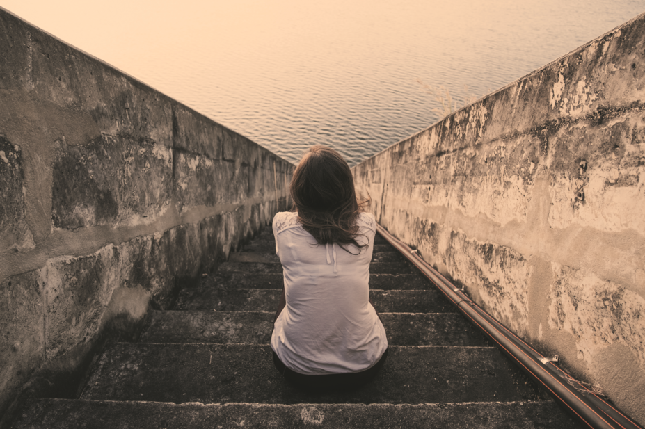 Imagery of mental illness: woman sits on stairs looking out to sea