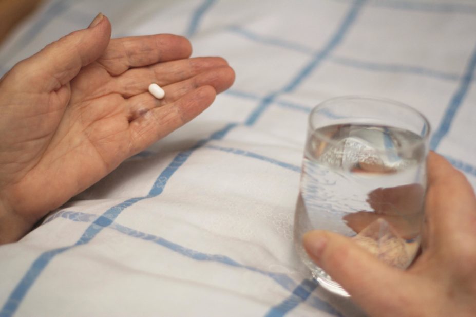 Close up of an elderly person's hands holding a glass of water and a pill