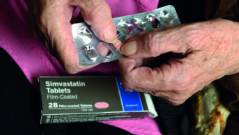 Elderly woman taking statin tablet out of blister pack, Simvastatin
