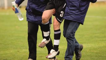 An injured player is carried out of a field with the help of two other people