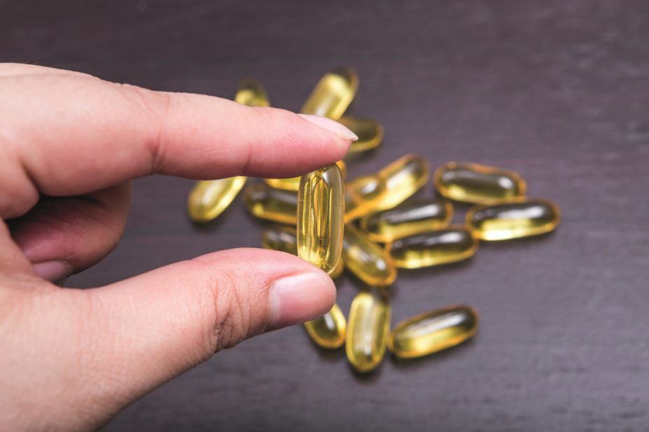 Hand holding fish oil capsule which is rich in omega-3 fatty acids