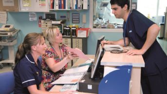 Hospital doctor and nurse talking to a discharge coordinator on a ward