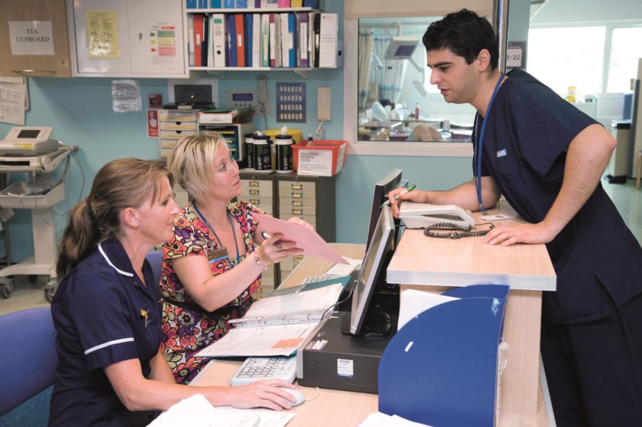 Hospital doctor and nurse talking to a discharge coordinator on a ward