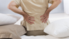 Older man with low back pain sitting on a bed