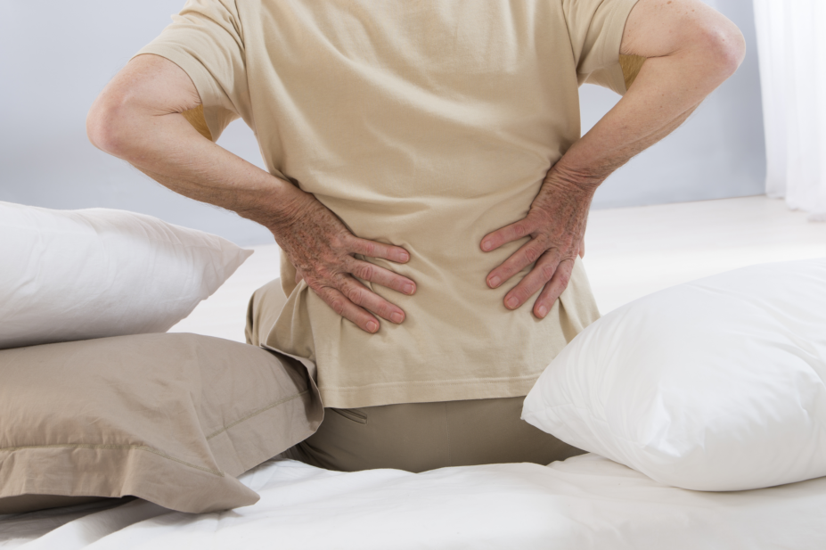 Older man with low back pain sitting on a bed