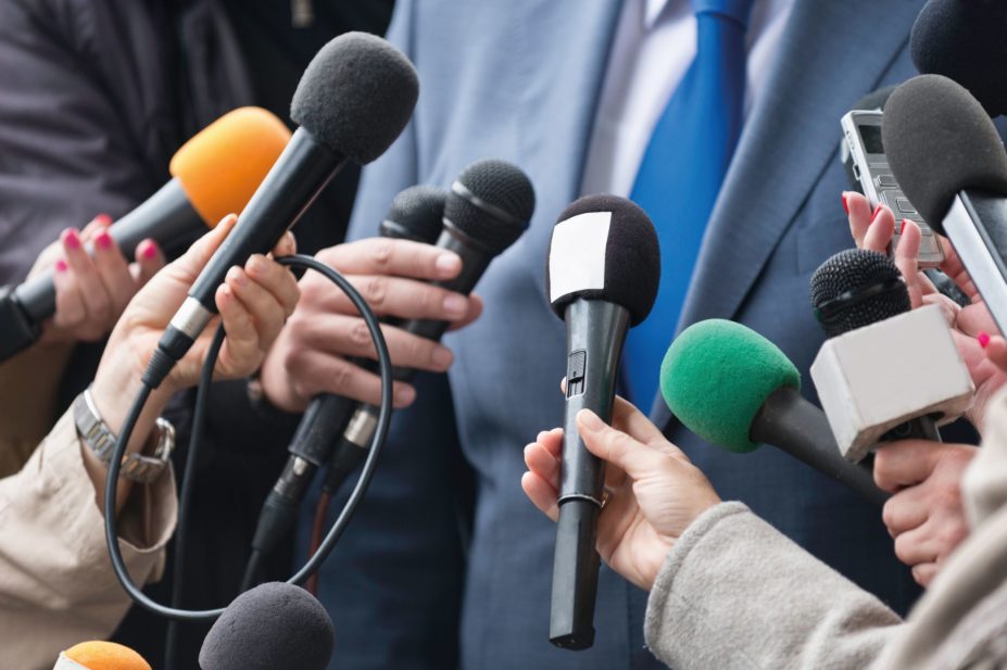 Image of a media press conference with journalists holding up microphones