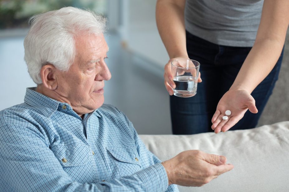 older man taking pills from carer
