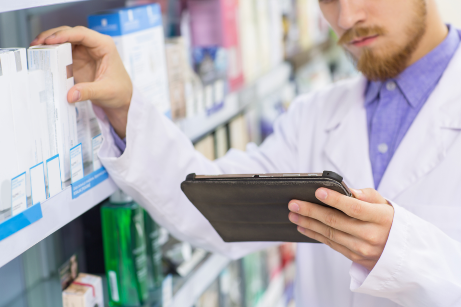 Man holding tablet computer while pulling an item from a pharmacy's shelf