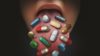 Close up of a person sticking their tongue out with lots of pills in their moth
