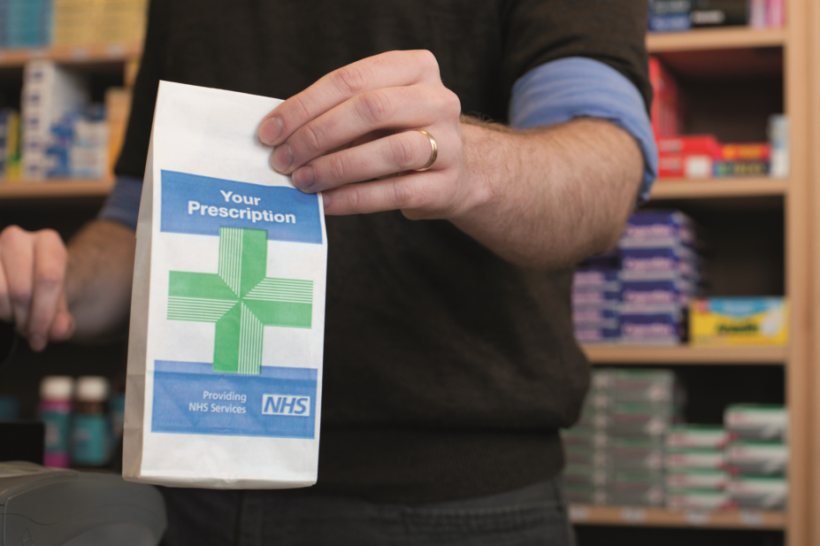 Pharmacist holding out an NHS prescription bag