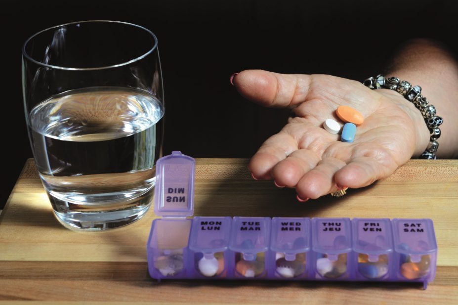 Elderly woman holds a handful of pills with a pillbox beside her
