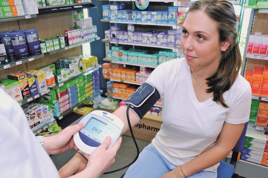 Leaders warn that the government’s proposed reduction in funding may prevent wider access to public health services through community pharmacies. Pictured image, a pharmacist takes a woman's blood pressure