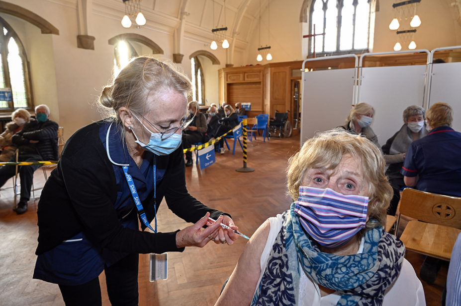 pharmacist giving older woman vaccine in village hall
