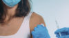 gloved hands holding vaccine, placing cotton wool on woman's arm