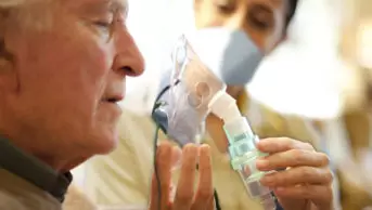 Woman in PPE mask helping older man with his breathing