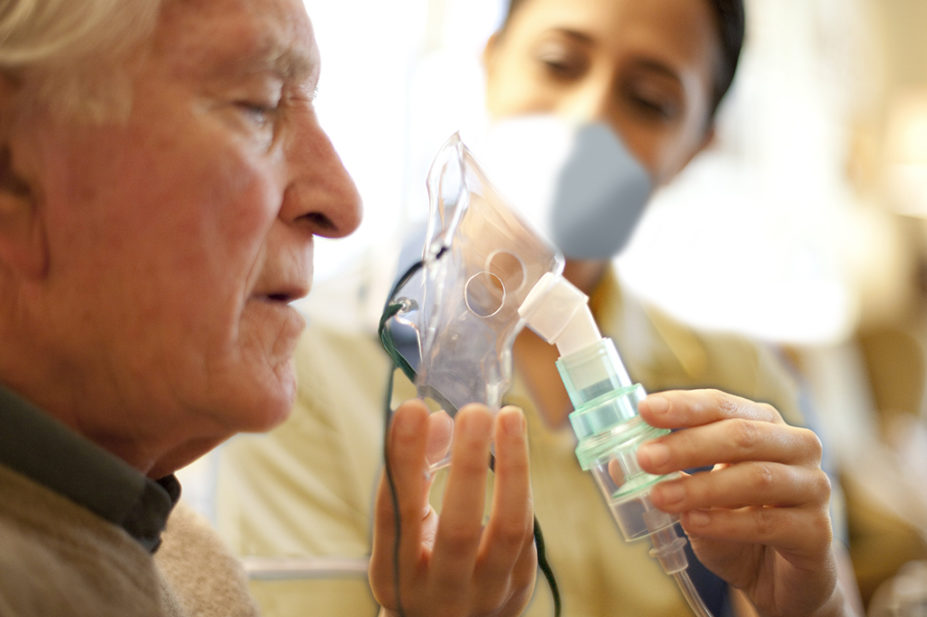Woman in PPE mask helping older man with his breathing