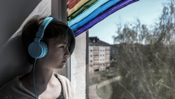 Photograph of a girl looking out of the window, which has a rainbow painted onto it