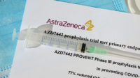 A syringe is placed on a document with the AstraZeneca logo