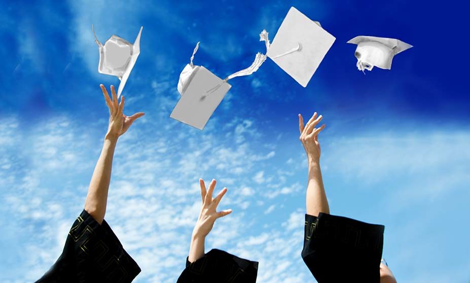 Photo of hands throwing white mortar board into the air at a graduation