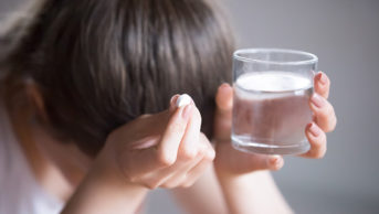 Woman holding headache medication and glass of water