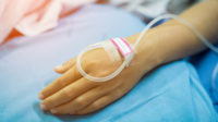 A hand with a cannula in it on a hospital bed