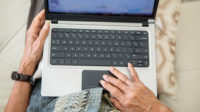 Close up of an older man's hands typing on the laptop computer keyboard at home
