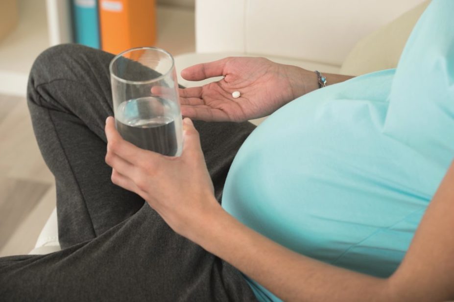 pregnant woman holding pill and glass of water