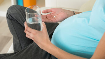 A mid section of a pregnant woman taking a tablet