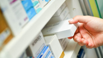A pharmacist's hand holding medicine box in pharmacy