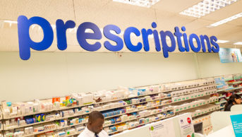 black male pharmacist behind prescriptions counter