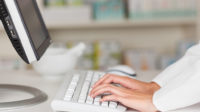 close up of pharmacist's hands typing on computer
