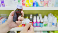 Hand holding a cough syrup bottle in pharmacy drugstore.