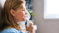 Young woman doing inhalation with steam nebulizer at home.