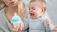 baby crying and pushing away bottle of milk