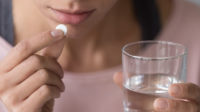 woman taking round white pill with water
