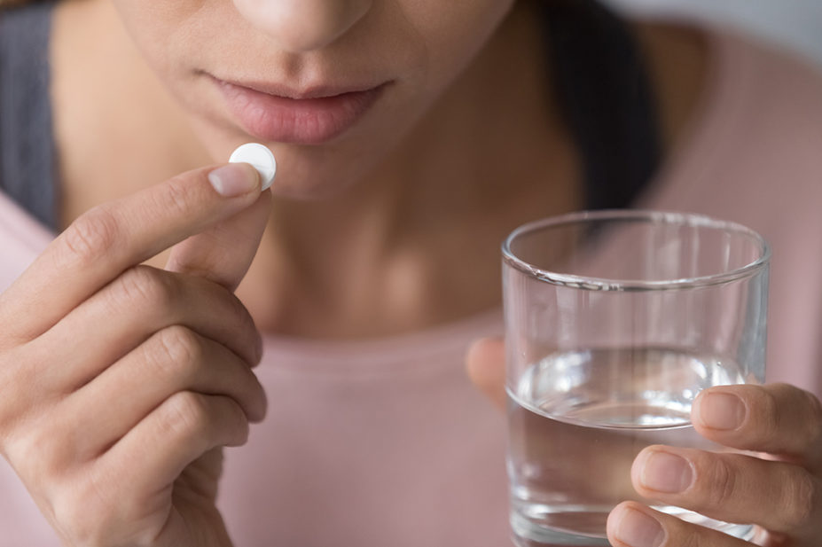 woman taking round white pill with water