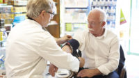 pharmacist taking older man's blood pressure