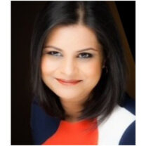 Adrusha smiles in front of a dark background, wearing a red white and navy top