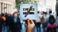 Hand holding equality symbol with a blurred crowd in the background