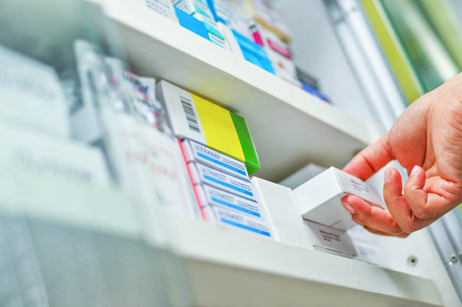 pharmacist's hand taking white box off medicines shelf
