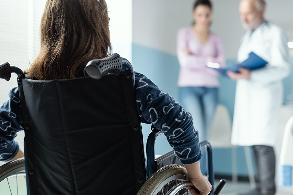 Girl in wheelchair at hospital, with parent and doctor talking in background
