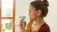 Young woman inhaling from nebuliser as part of cystic fibrosis treatment.
